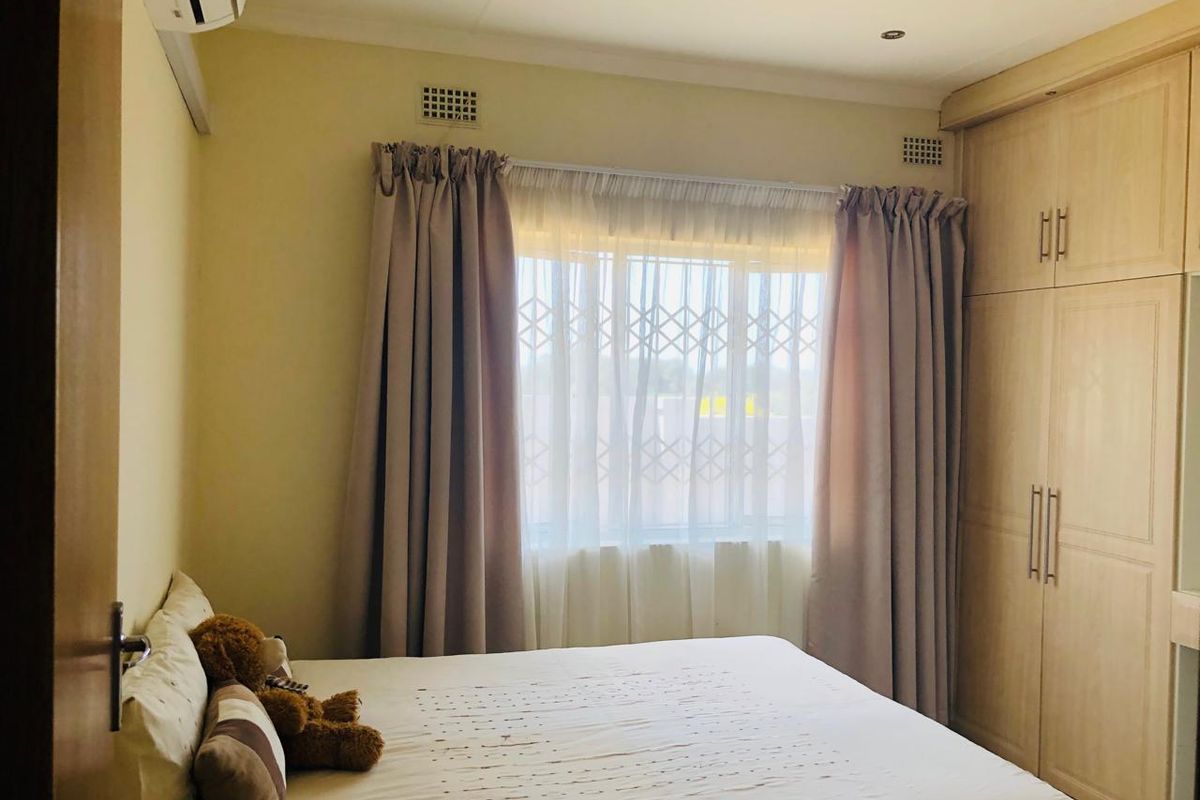 A well-maintained bedroom featuring built-in cupboards, an air conditioning unit, and a security gate on the window.