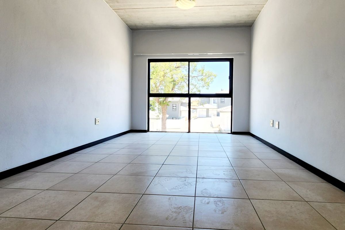 An empty bedroom featuring tiled flooring, an exposed concrete ceiling, and a large sliding glass door providing natural light.