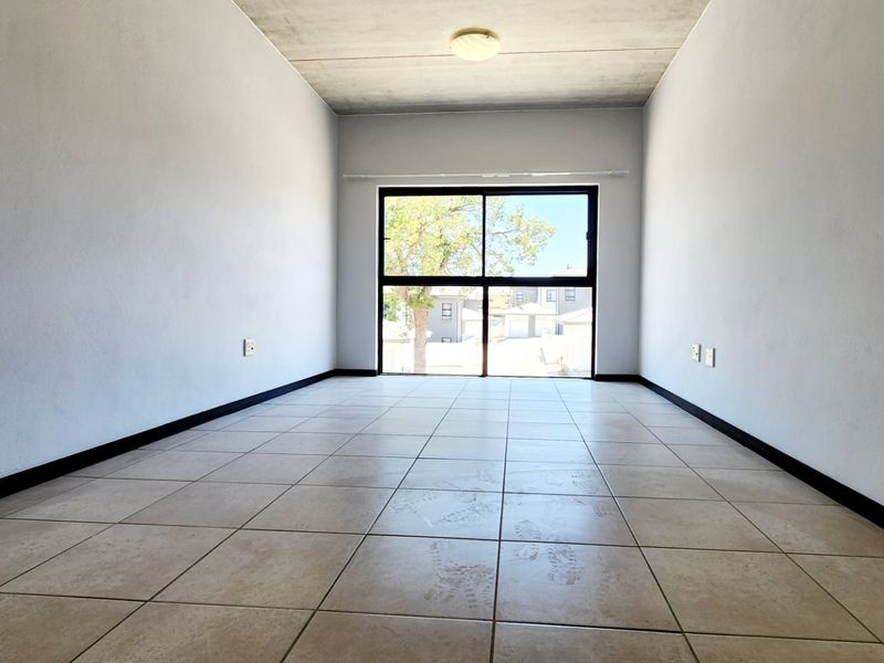 An empty bedroom featuring tiled flooring, an exposed concrete ceiling, and a large sliding glass door providing natural light.