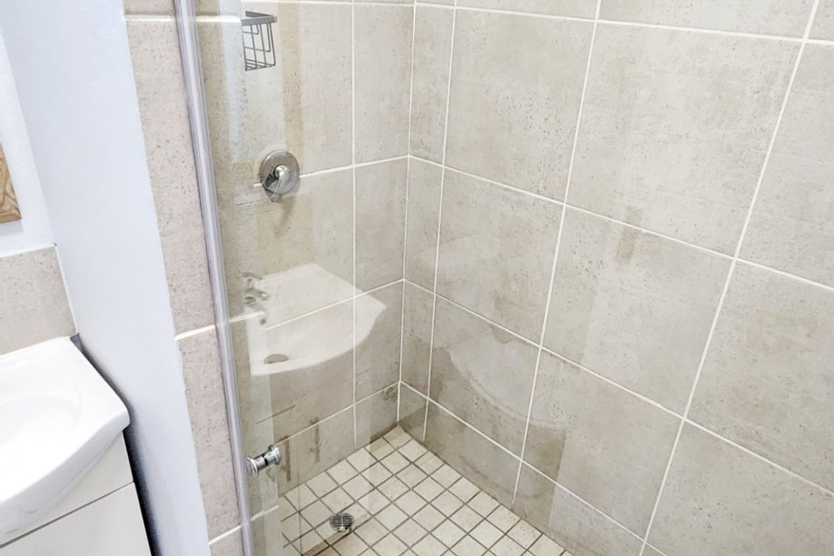 A functional bathroom featuring a glass-enclosed shower with neutral wall tiles and a vanity cabinet with a basin.