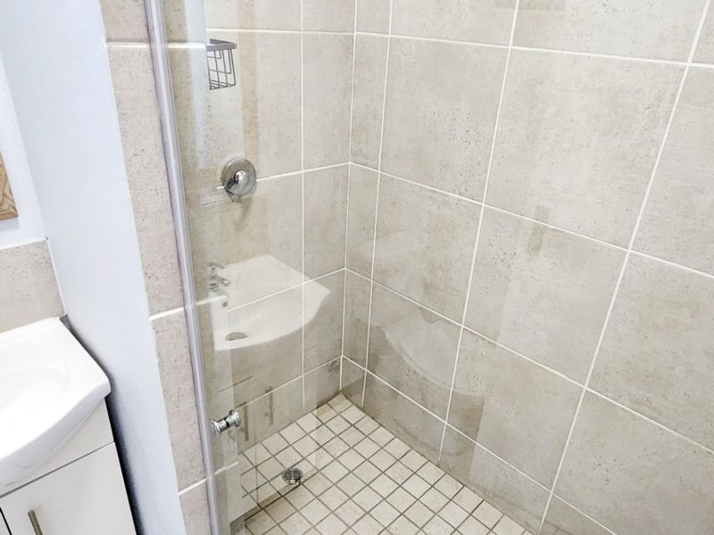 A functional bathroom featuring a glass-enclosed shower with neutral wall tiles and a vanity cabinet with a basin.