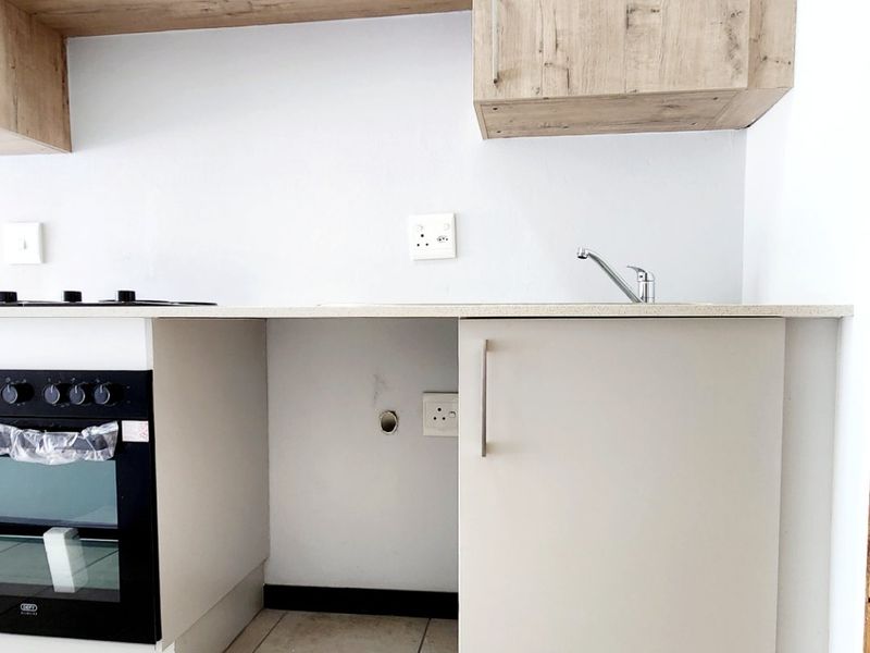 A compact kitchen area featuring built-in cabinetry, a modern oven and hob, and tiled flooring, with an open space ready for an under-counter appliance.