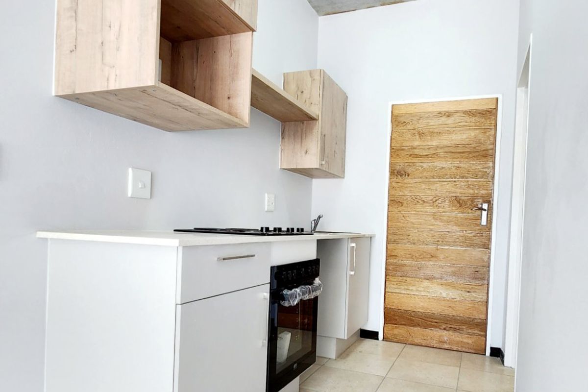 A modern, compact kitchen featuring light wood cabinetry, built-in oven and hob, tiled flooring, and a unique exposed concrete ceiling.