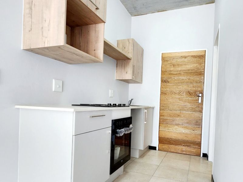 A modern, compact kitchen featuring light wood cabinetry, built-in oven and hob, tiled flooring, and a unique exposed concrete ceiling.