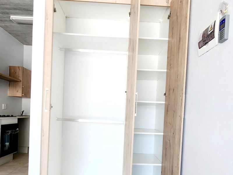Open plan living area featuring a modern built-in wardrobe with light wood finish, tiled flooring, and an exposed concrete ceiling.