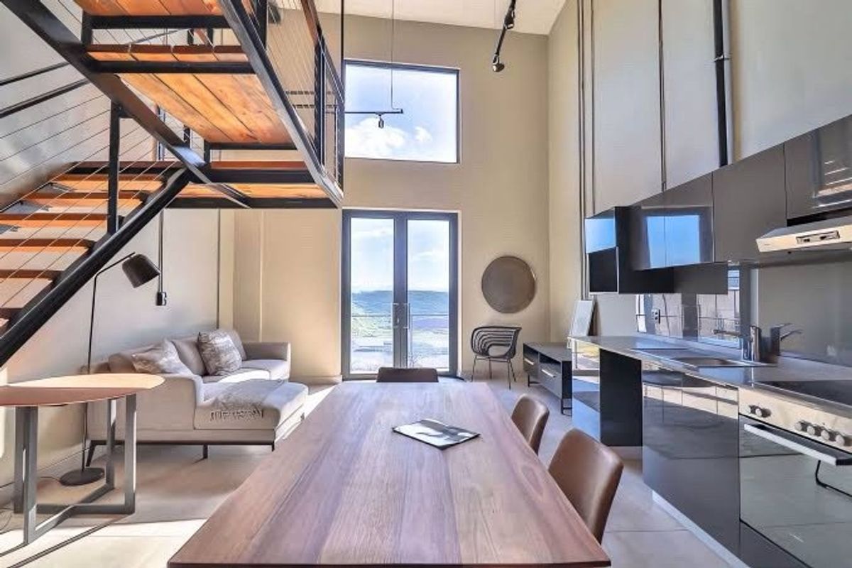 Modern open-plan living area featuring a striking industrial staircase, high-gloss kitchen cabinetry, and double doors leading to an outdoor balcony with scenic views.