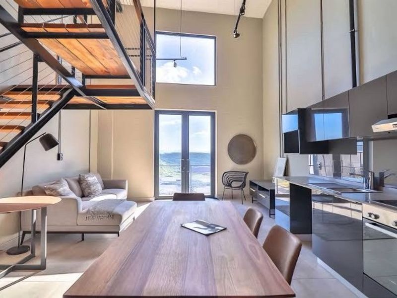 Modern open-plan living area featuring a striking industrial staircase, high-gloss kitchen cabinetry, and double doors leading to an outdoor balcony with scenic views.
