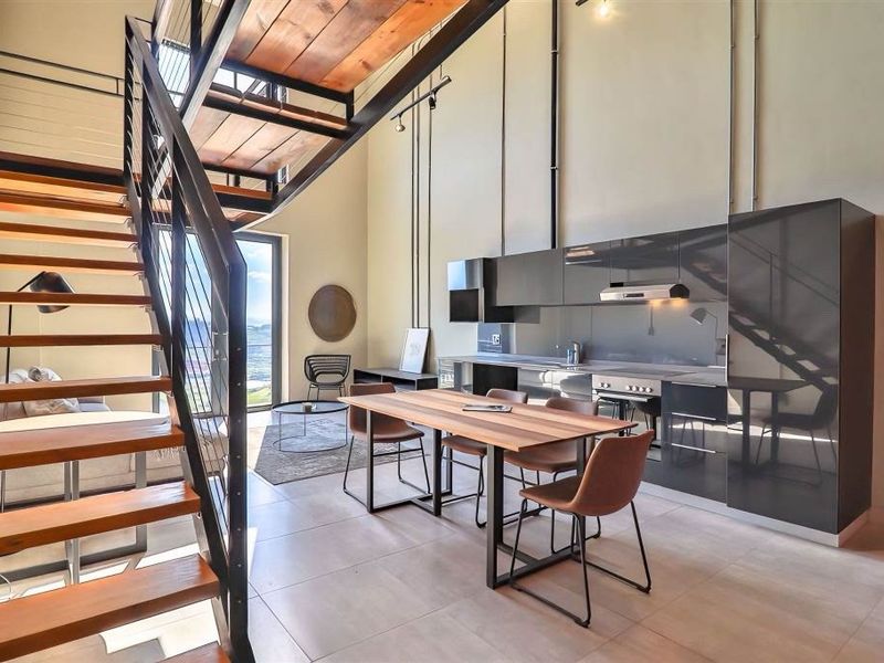 Modern open-plan living area featuring a sleek kitchen with high-gloss cabinetry, integrated appliances, and a striking industrial-style staircase leading to a mezzanine level.
