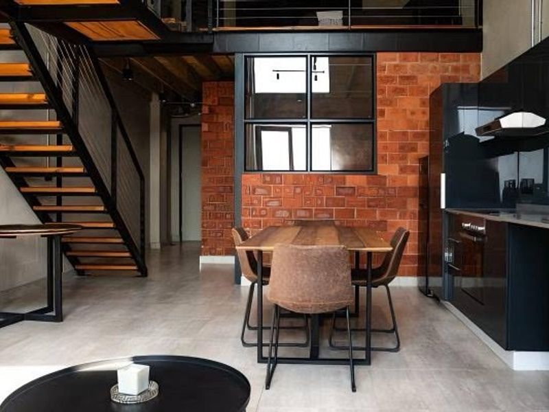 Modern industrial open-plan living area featuring exposed brickwork, a striking staircase, and a sleek, contemporary kitchen with integrated appliances.