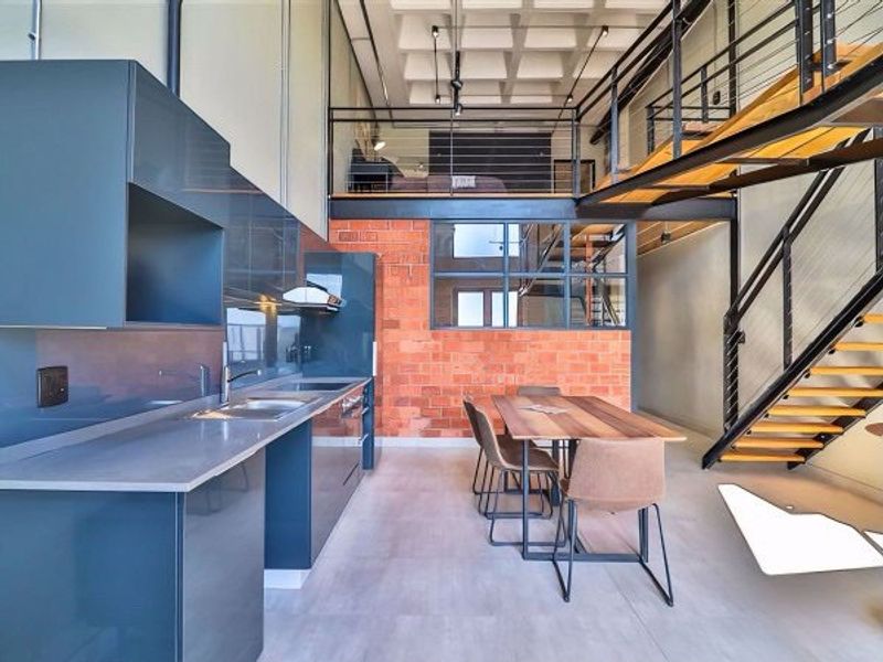 Modern open-plan apartment featuring a sleek kitchen, exposed brick wall, and a mezzanine level accessed by a contemporary steel staircase.