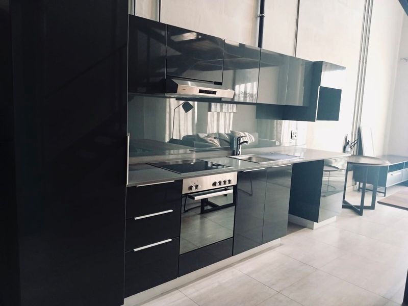 Modern kitchen featuring sleek glossy black cabinetry, integrated oven, electric hob, extractor fan, and a reflective mirror splashback with stone countertops.