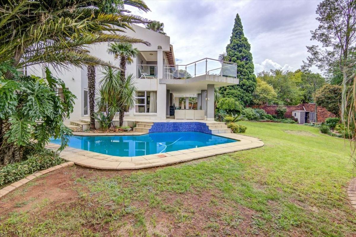 Rear view of the property featuring a swimming pool, covered patio, elevated balcony with glass balustrades, and a spacious landscaped garden.