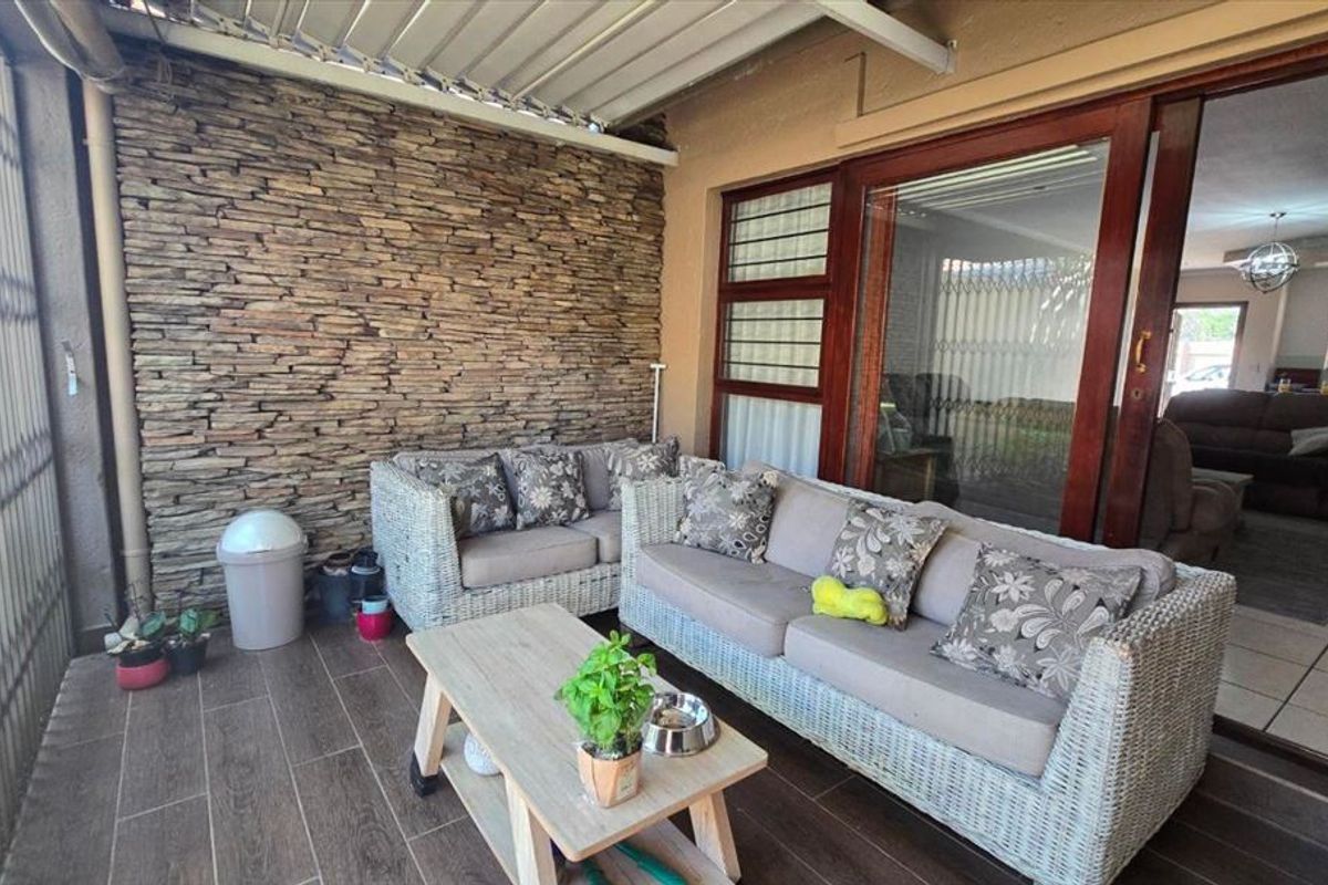 A covered patio area featuring a decorative stone cladding wall, wood-look tiled flooring, and large sliding glass doors providing access to the interior living space.
