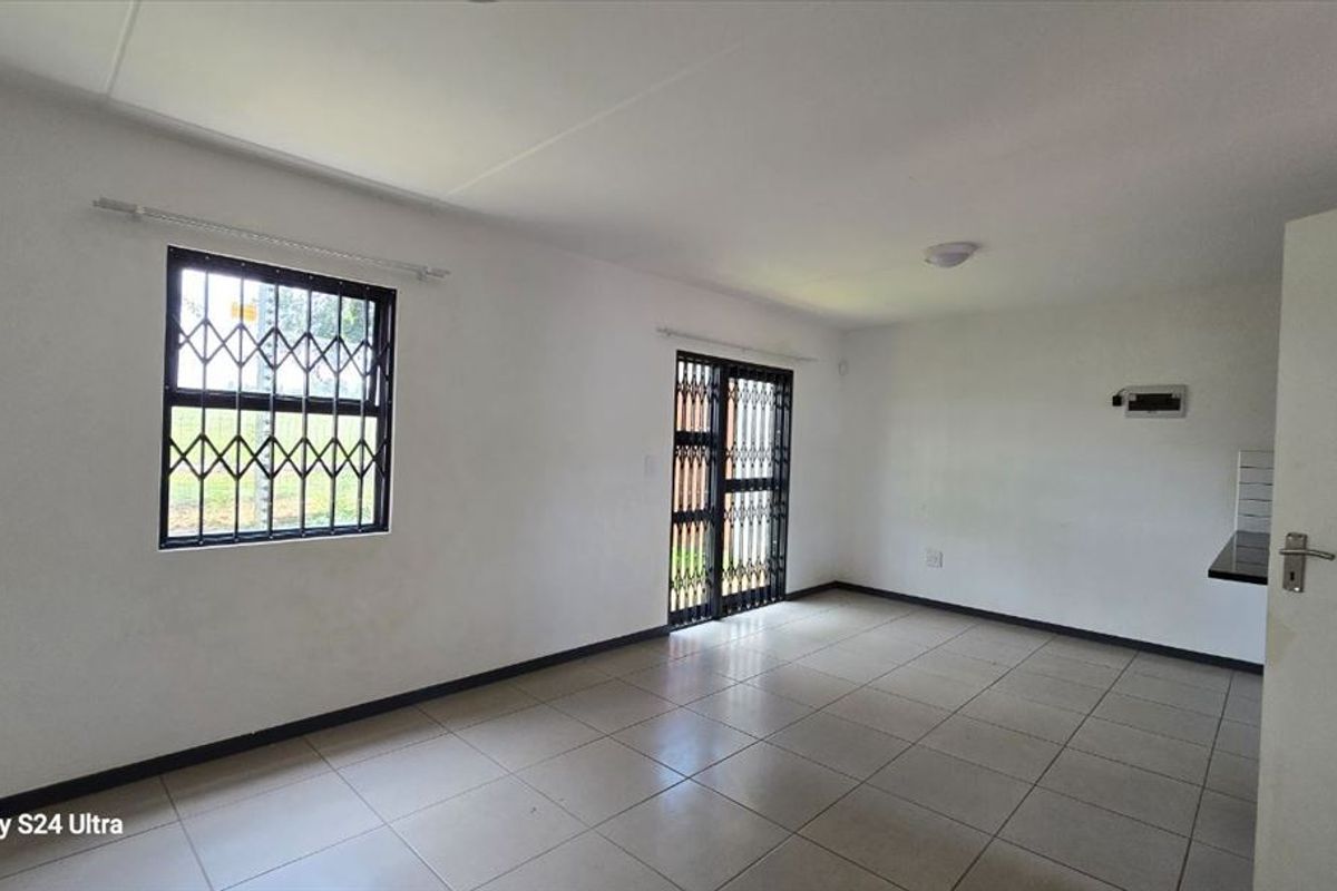 An empty open-plan living area featuring tiled flooring, security gates on the doors, and burglar bars on the windows.