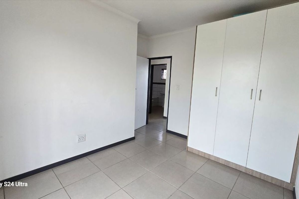 A clean, empty bedroom featuring neutral tiled flooring and built-in white cupboards, offering a blank canvas for personalization.
