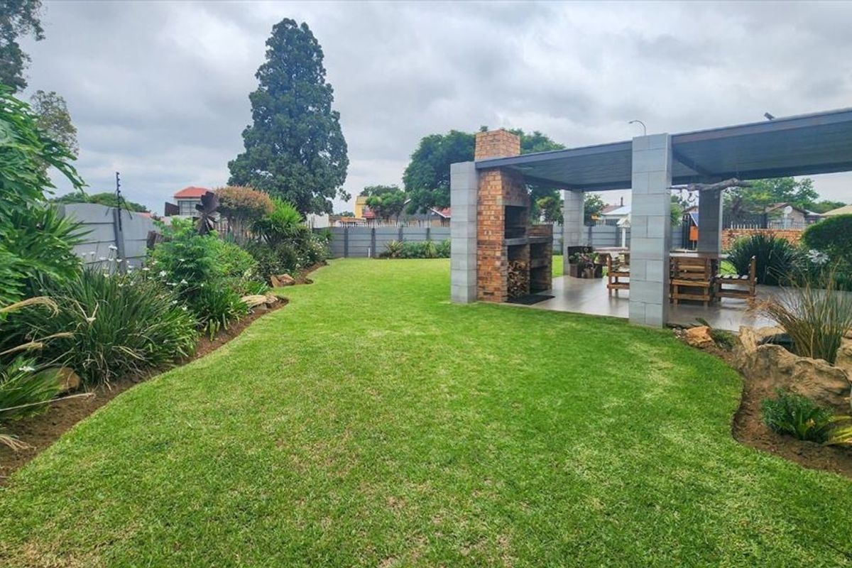 A well-maintained rear garden featuring a spacious lawn, landscaped borders, and a covered patio area with a built-in brick braai.