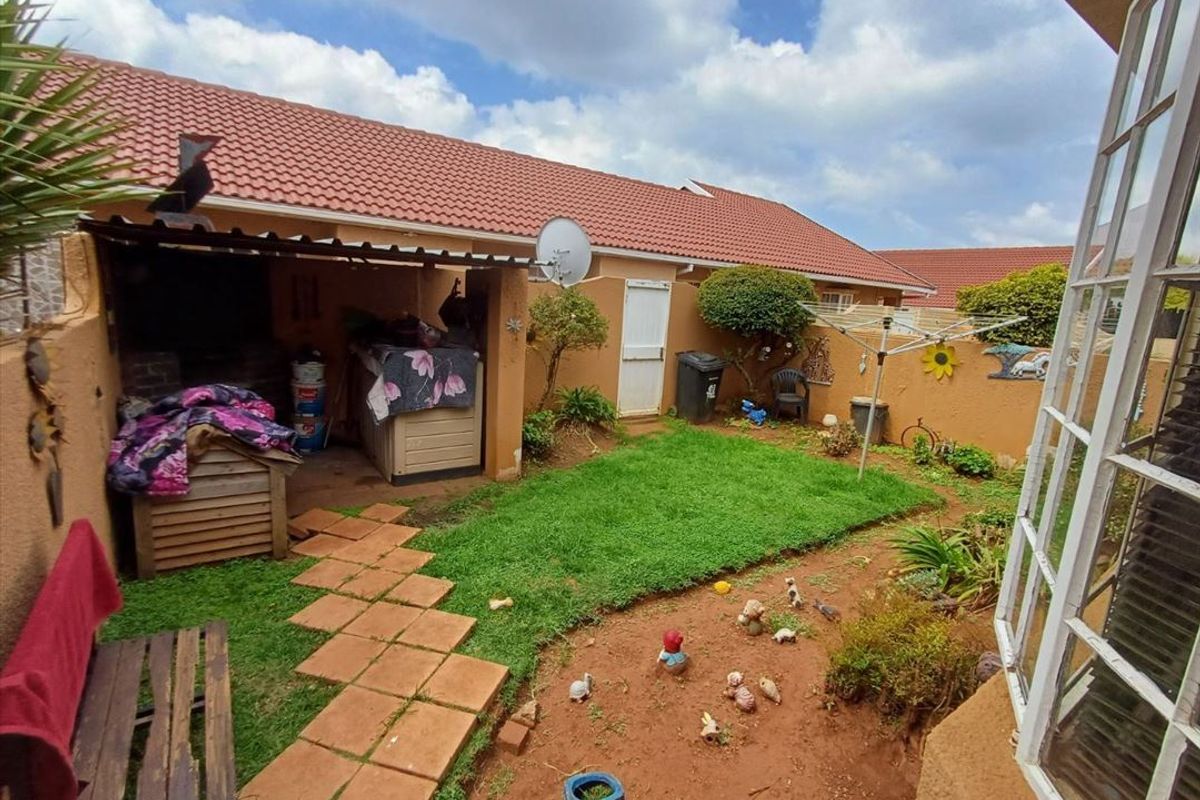 A rear garden area featuring a covered patio with a built-in braai, paved walkway, and boundary walling.