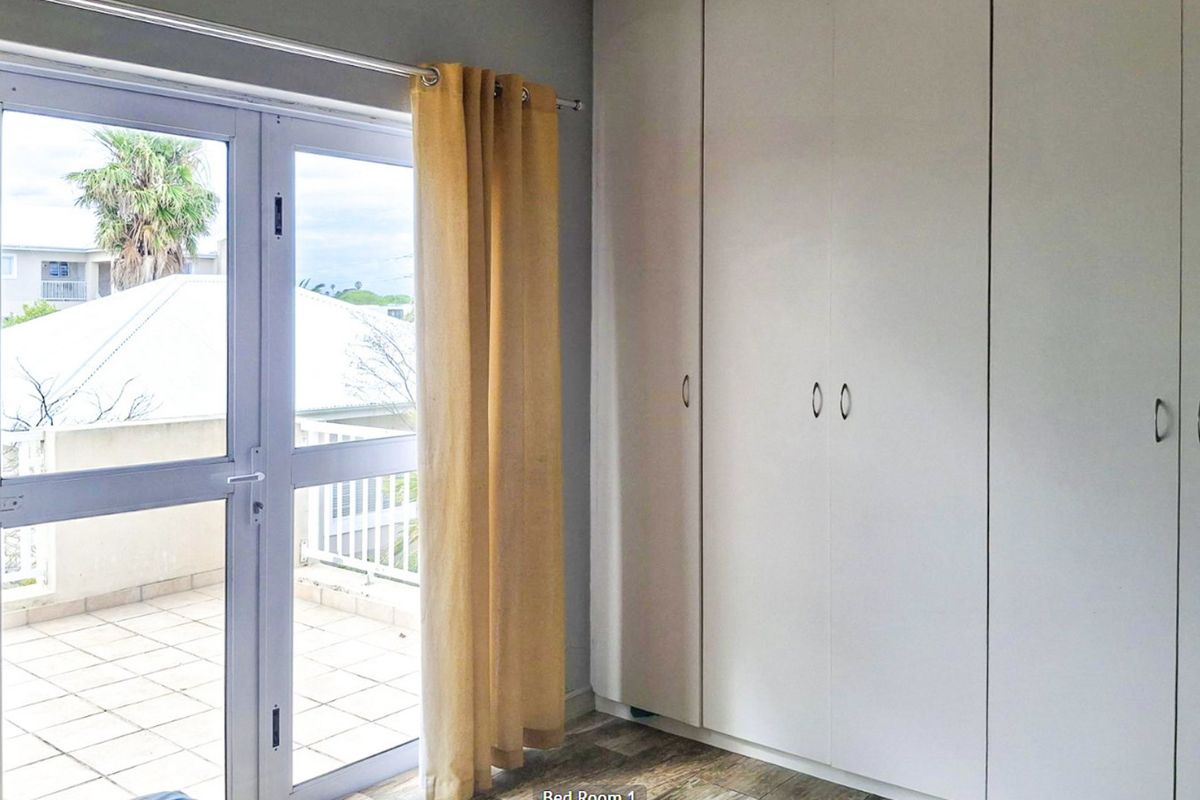 A bright bedroom featuring built-in cupboards, laminate flooring, and a glass door providing access to an outdoor balcony area.