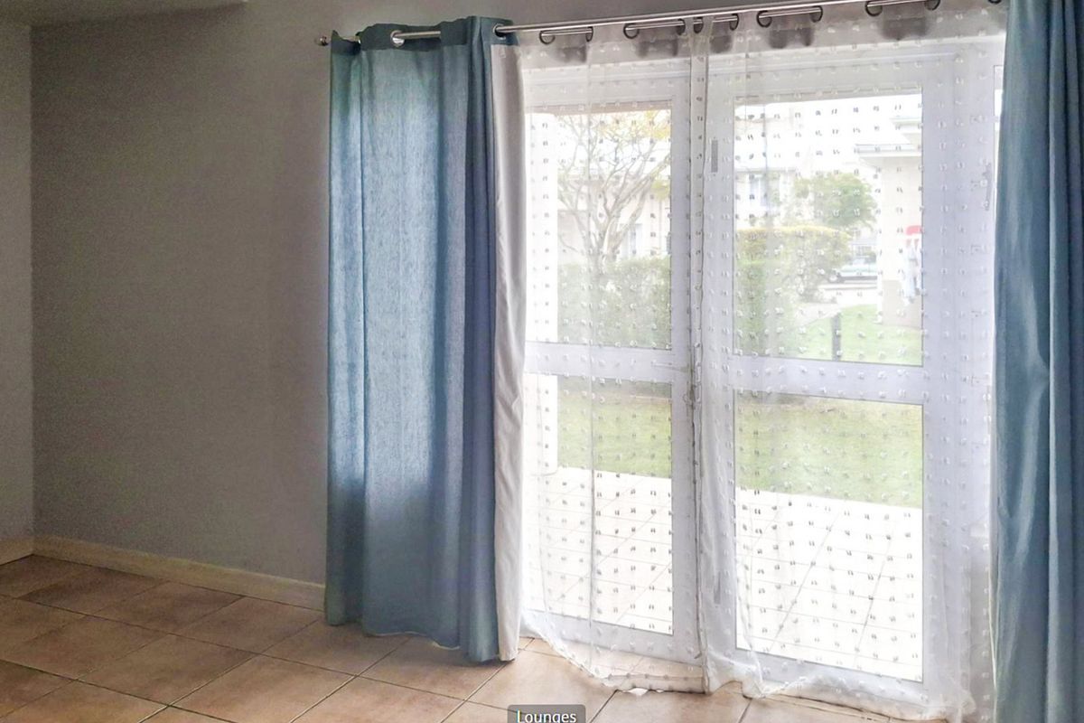An empty living room featuring tiled flooring and a double glass door providing access to the exterior.