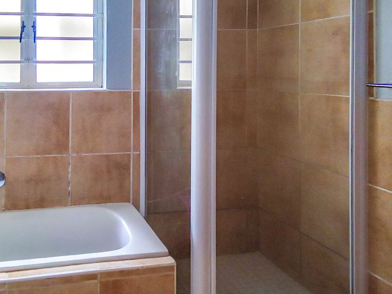 A functional bathroom featuring a built-in bathtub and a separate shower enclosure with neutral wall tiling and a window for natural light.