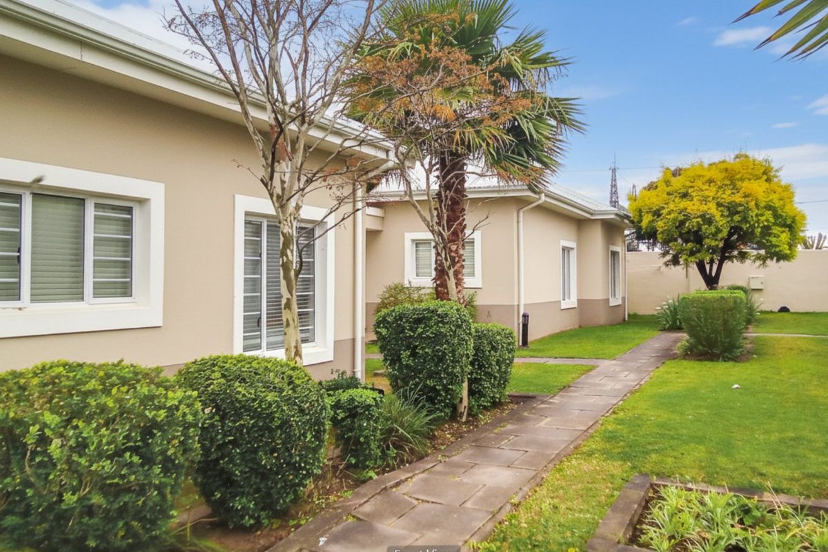 A well-maintained rear exterior view of the apartment complex featuring a paved walkway, manicured lawn, and established garden landscaping.