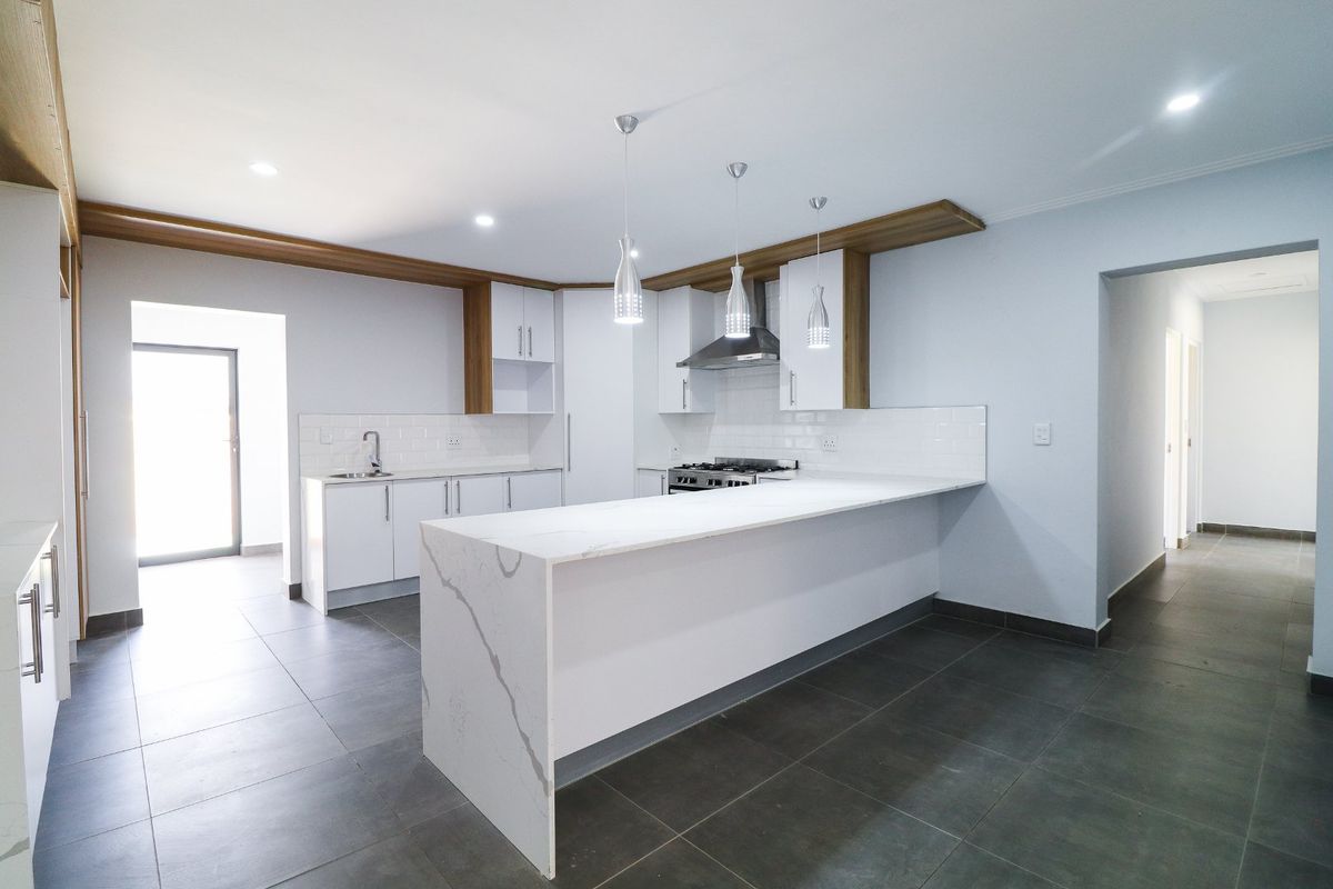 Modern kitchen featuring a large marble-look island, white cabinetry, subway tile backsplash, stainless steel gas stove, and sleek pendant lighting.