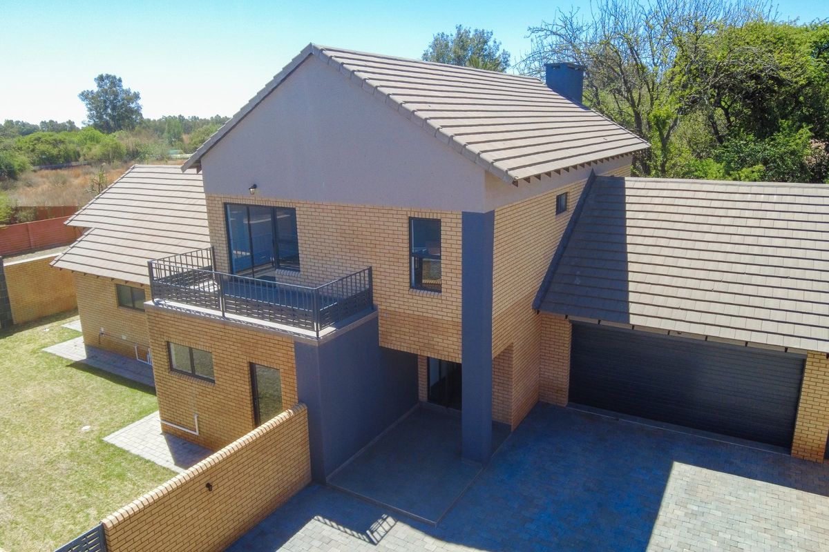 Aerial view of a modern townhouse featuring a face-brick facade, tiled roof, balcony, and an integrated garage with paved driveway.