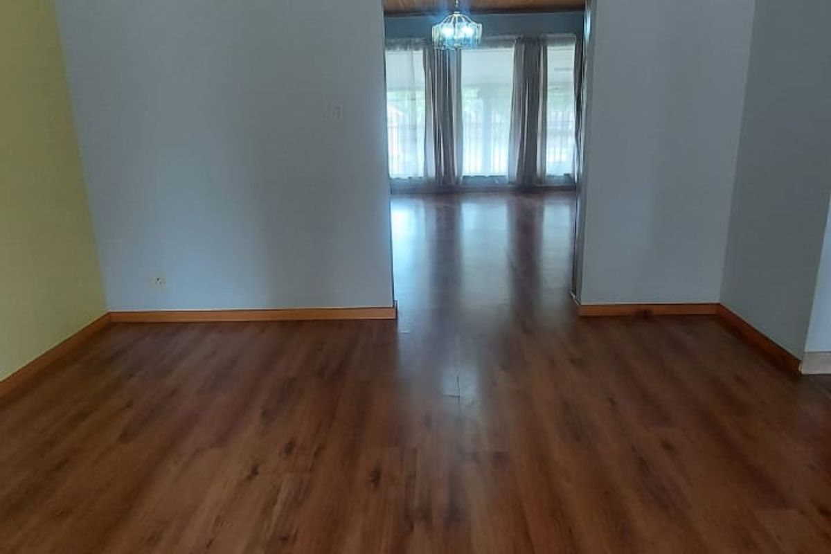 Spacious living area featuring warm-toned laminate flooring and a distinctive timber-clad ceiling, connected to an adjacent room through a classic archway.