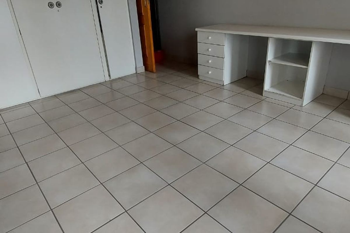 A spacious bedroom featuring tiled flooring, a timber ceiling, built-in cupboards, and a convenient built-in desk area.