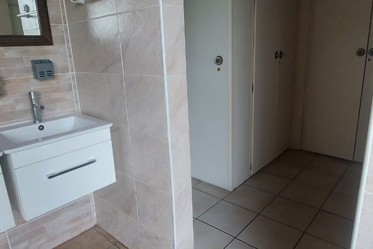 A functional bathroom featuring a wall-mounted vanity, tiled surfaces, and integrated storage cupboards with a timber ceiling finish.