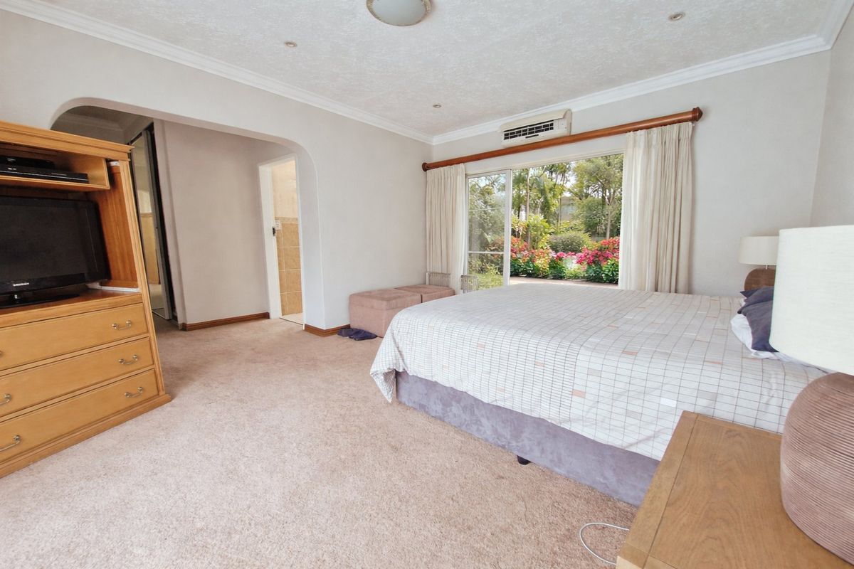 Spacious bedroom featuring carpeted flooring, a wall-mounted air conditioning unit, and sliding glass doors providing direct access to the garden.