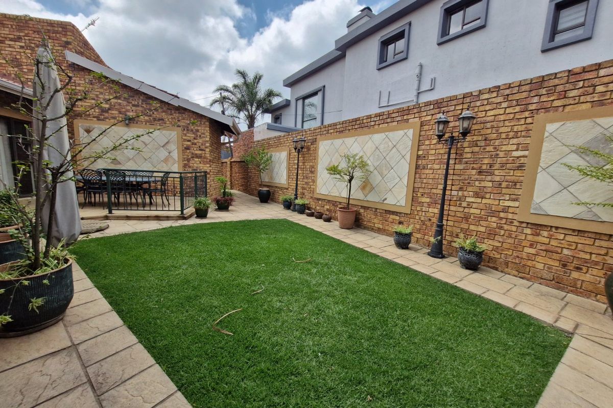 A well-maintained rear courtyard featuring a paved patio area, artificial lawn, and decorative brick boundary walls with stone inlay.