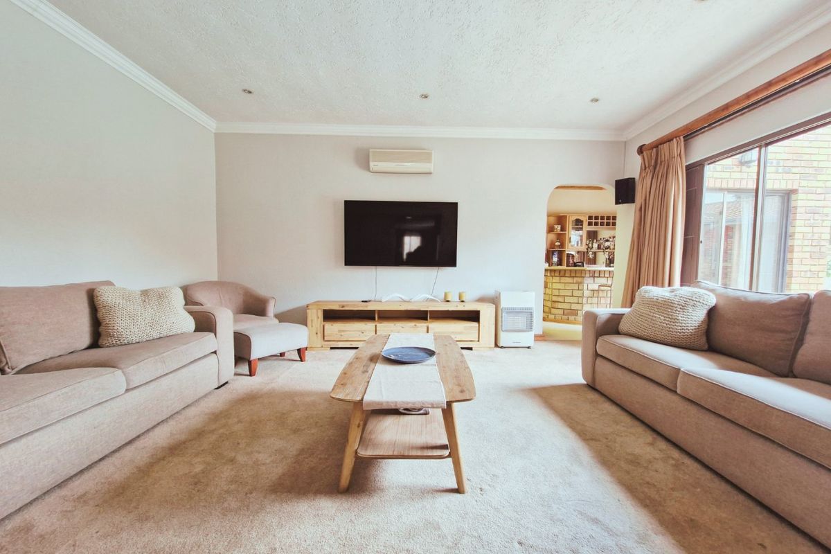 A comfortable living room featuring neutral carpeting, recessed lighting, and a wall-mounted air conditioning unit, with a view through to an adjacent bar area.