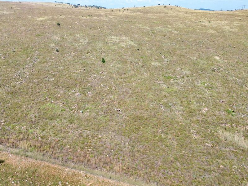 An aerial view of expansive, open grazing land featuring natural terrain and perimeter wire fencing.