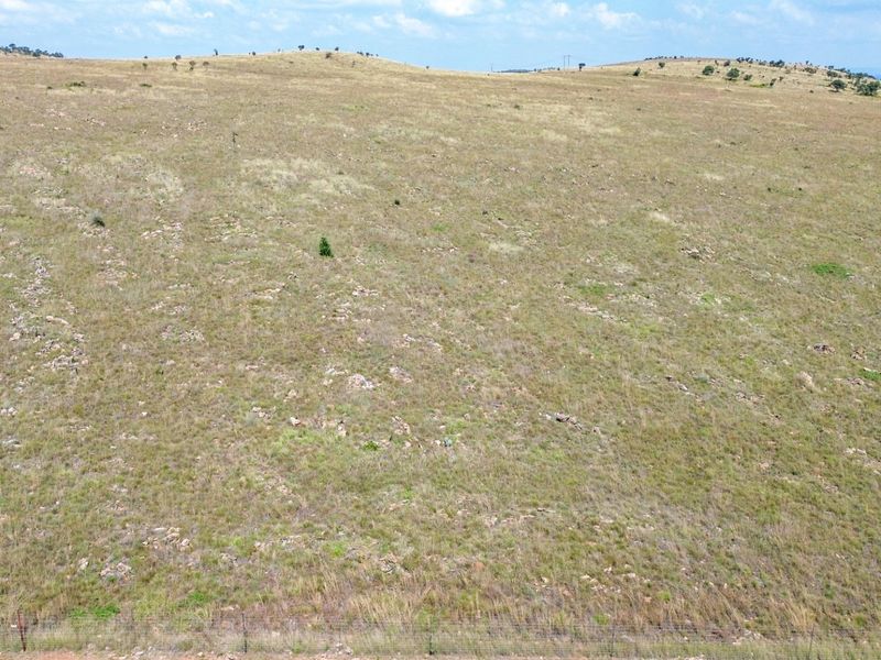 An aerial view of expansive, open grazing land featuring natural terrain and perimeter wire fencing.
