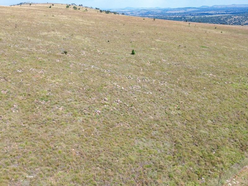 An aerial view of expansive, open grazing land on a farm, featuring natural terrain and perimeter wire fencing.