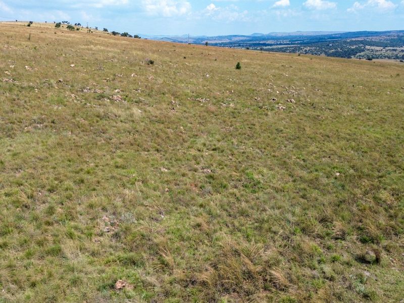 An expansive aerial view of open, undeveloped farm land with natural grass terrain and distant rolling hills.