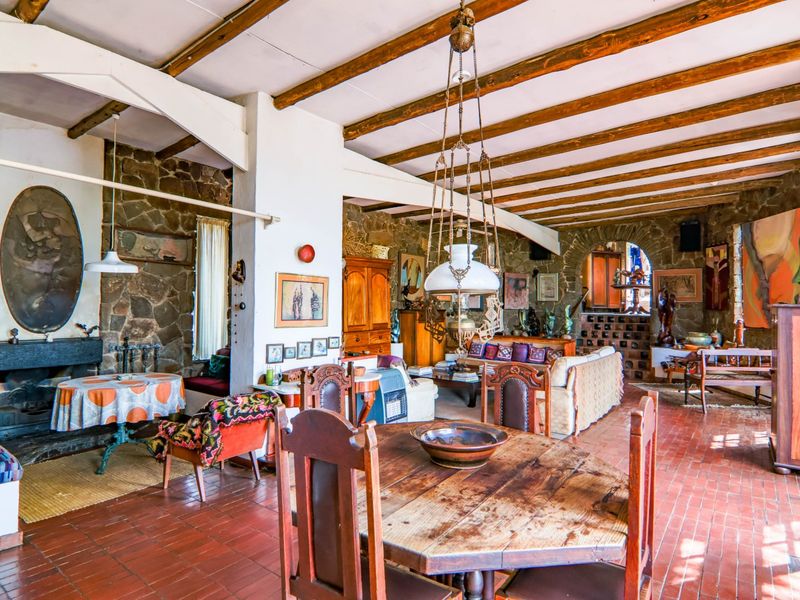 Spacious open-plan living and dining area featuring rustic stone walls, exposed timber ceiling beams, and traditional terracotta tile flooring with a built-in fireplace.