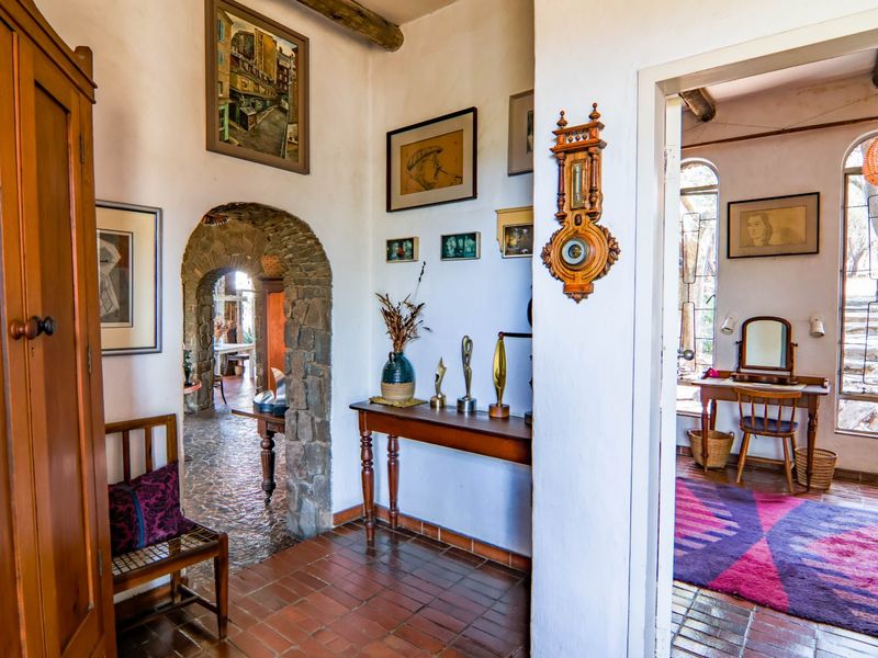A rustic hallway featuring traditional terracotta tile flooring, a distinctive stone archway, and exposed timber ceiling beams, connecting multiple living spaces.