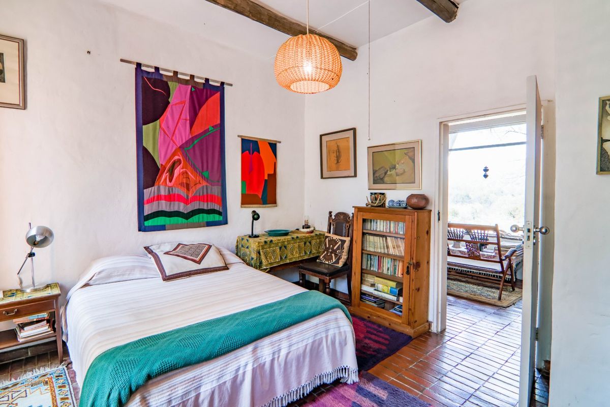 A rustic bedroom featuring exposed timber ceiling beams, terracotta tile flooring, and direct access to an outdoor patio area.