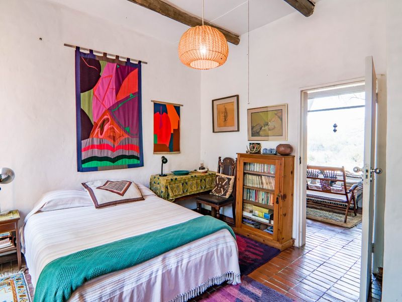 A rustic bedroom featuring exposed timber ceiling beams, terracotta tile flooring, and direct access to an outdoor patio area.