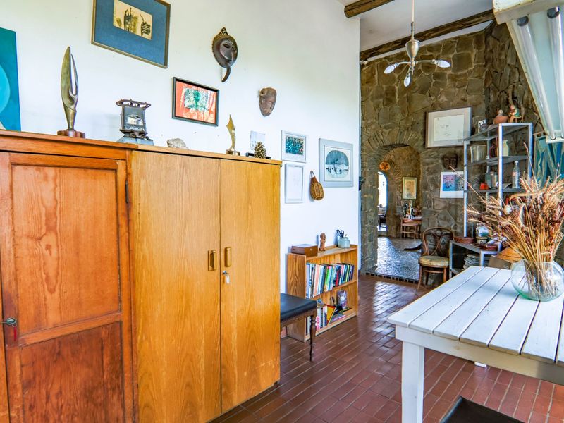 A rustic living area featuring a stone feature wall, an arched stone doorway, exposed ceiling beams, and traditional terracotta tile flooring.