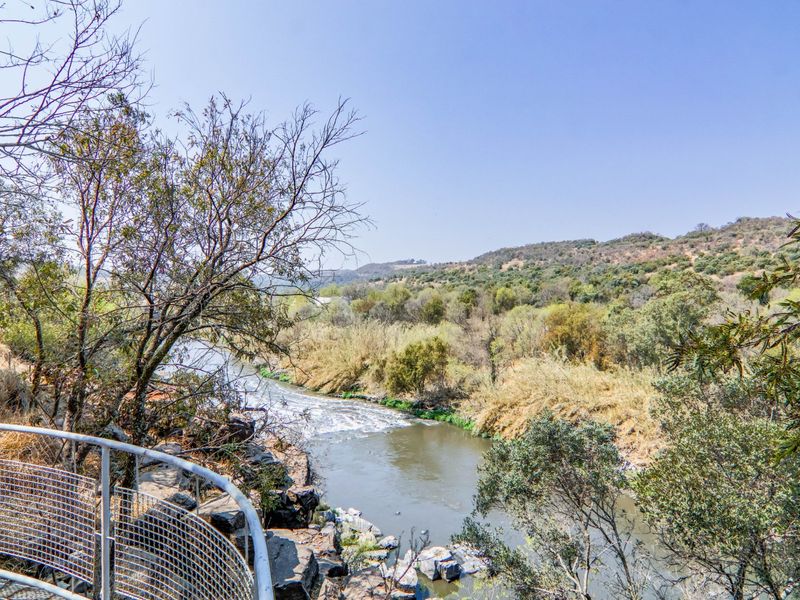 A scenic view overlooking a flowing river and natural landscape, featuring a metal safety railing in the foreground.