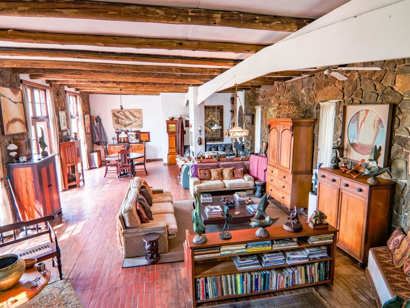 Spacious open-plan living and dining area featuring rustic exposed timber beams, a prominent stone feature wall, and warm terracotta tile flooring throughout.