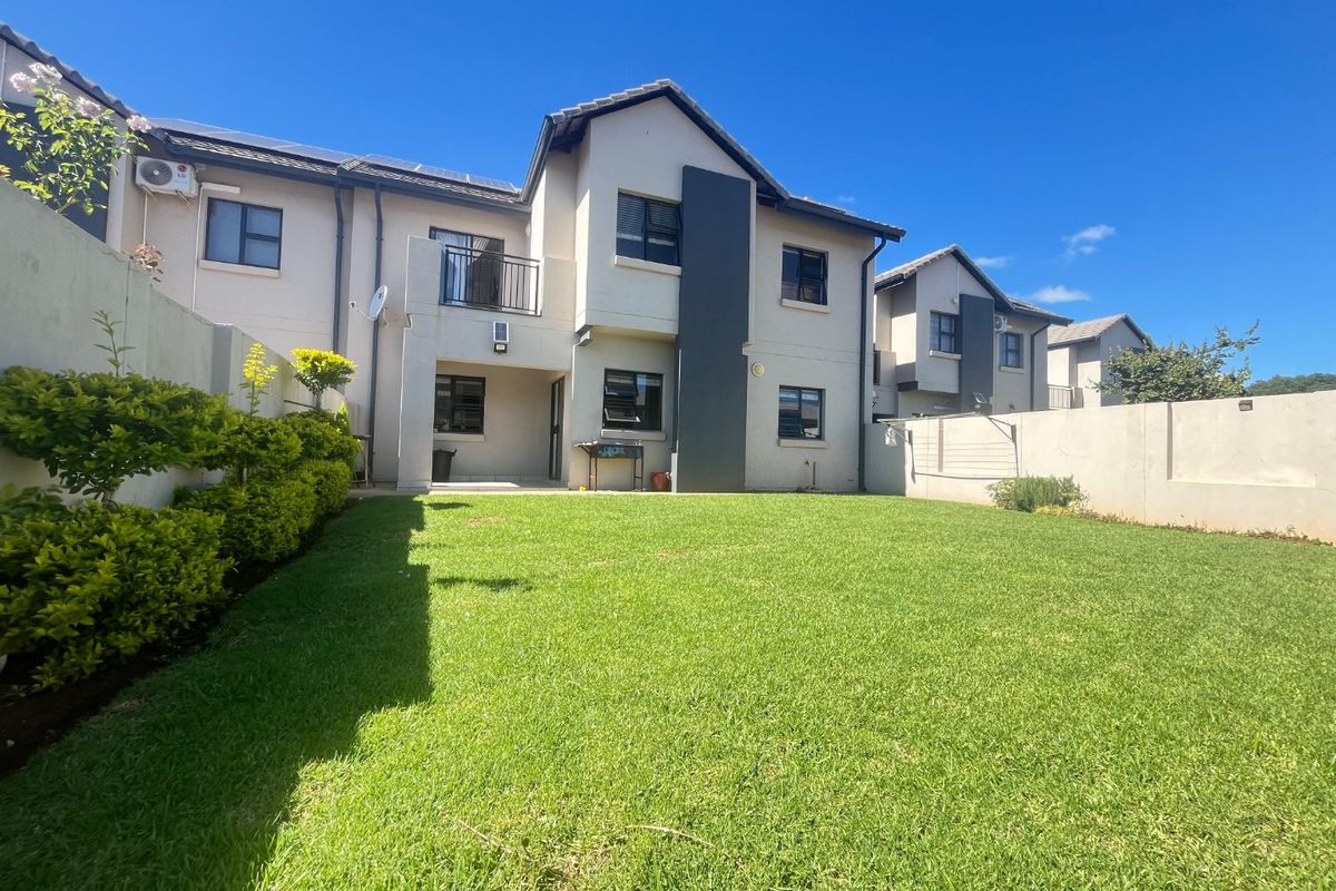 A well-maintained rear exterior view of a townhouse featuring a private lawn, landscaped garden, boundary walls, and a balcony.