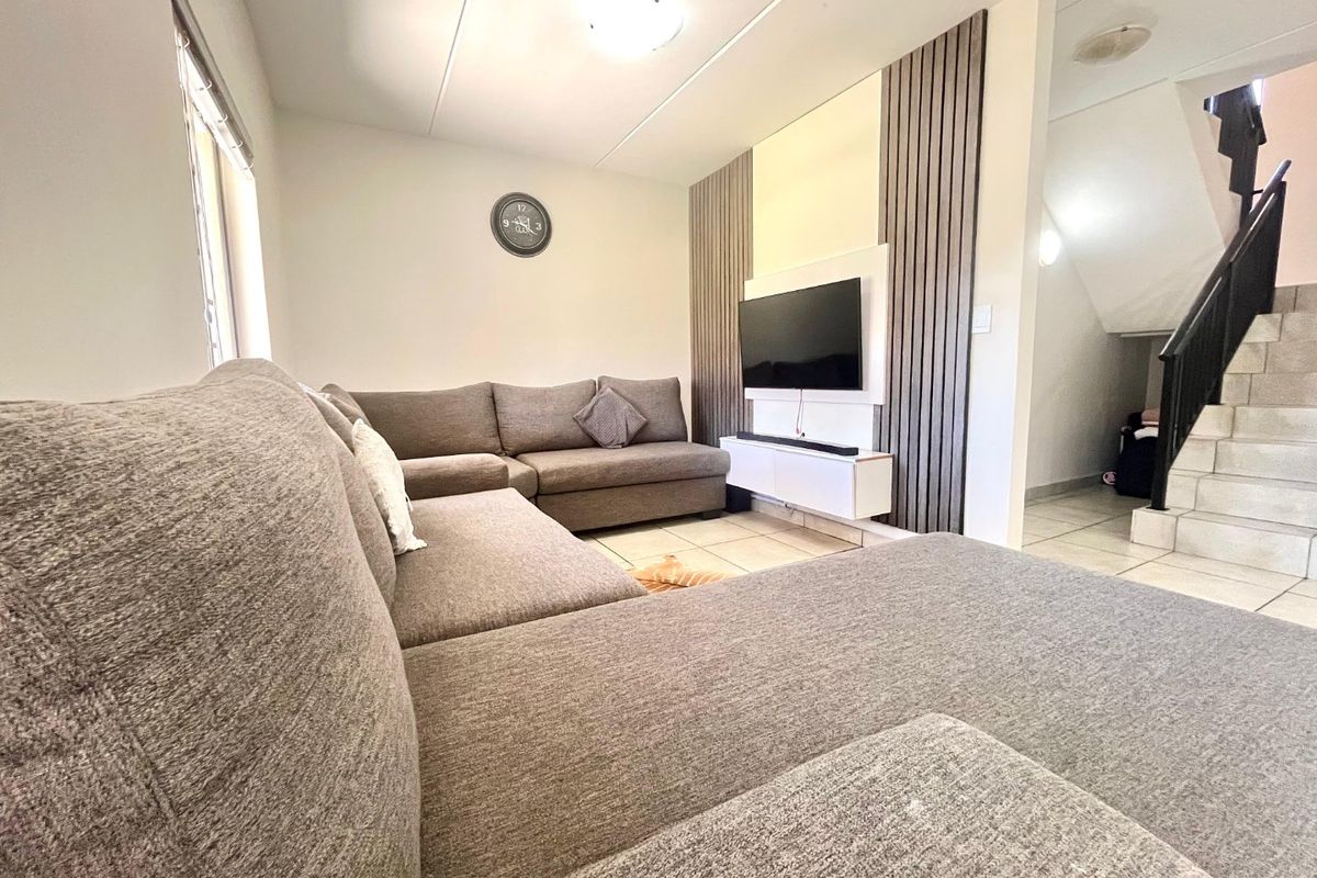 A comfortable living room featuring modern slatted timber wall paneling, tiled flooring, and an adjacent staircase with a metal balustrade.