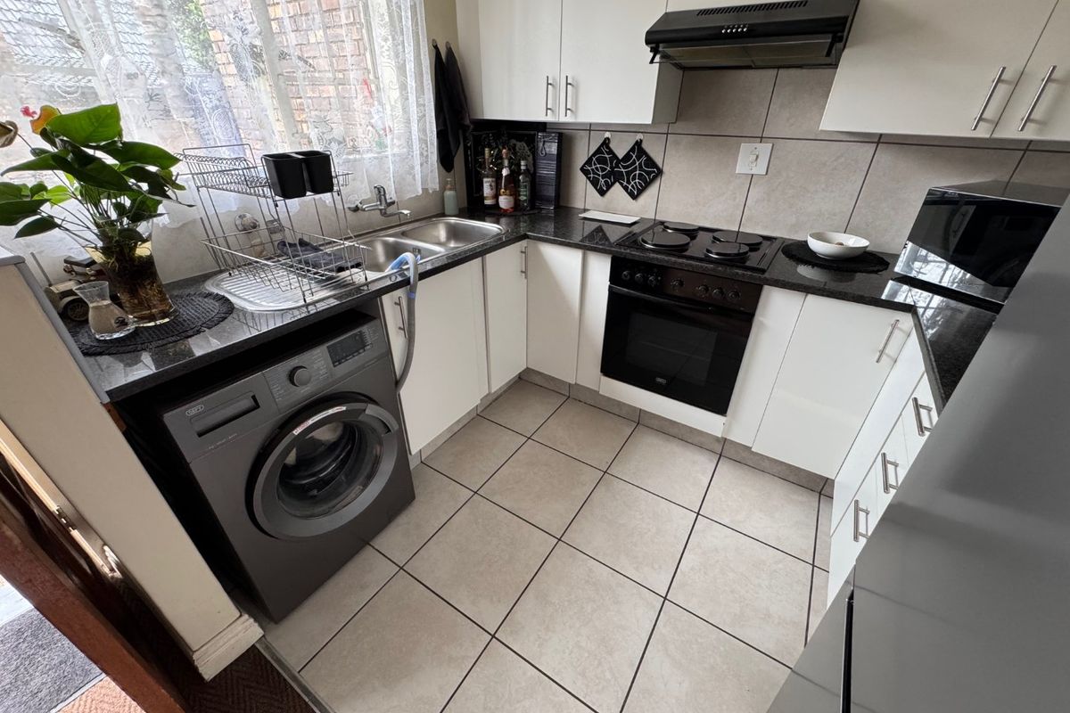 A functional kitchen featuring white cabinetry, granite countertops, a built-in oven with hob, and tiled flooring with integrated laundry plumbing.