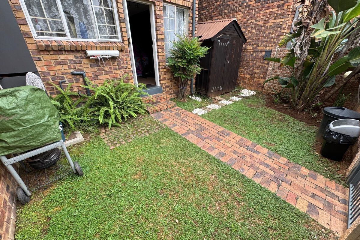 A rear courtyard area featuring brick paving, a small lawn, and a timber garden shed against a brick townhouse facade.