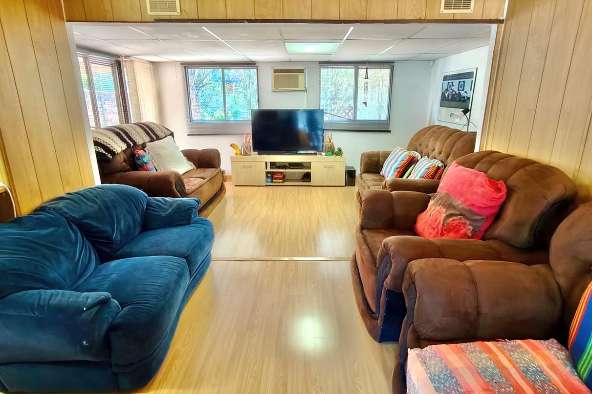 A living room featuring wood-panelled walls, laminate flooring, and a drop ceiling, offering a dated aesthetic suitable for modernization.