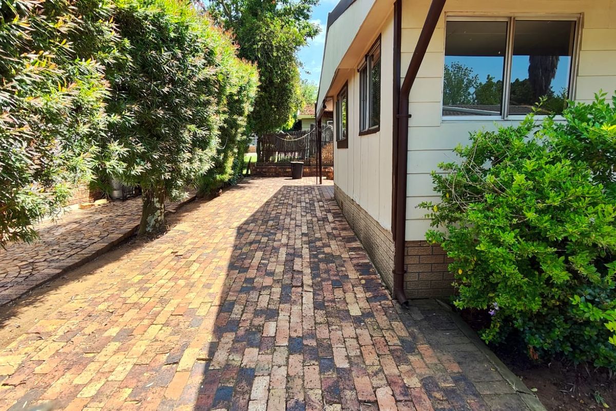 A side pathway featuring brick paving alongside the exterior wall of the apartment building, bordered by established hedges and greenery.